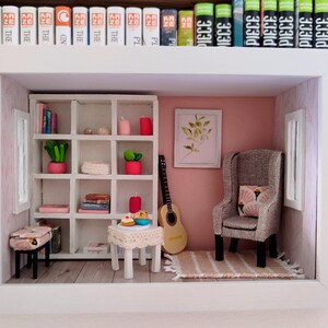 Può includere: Diorama di una stanza in miniatura con una parete rosa, scaffalature bianche e una chitarra. La scena comprende una piccola poltrona, un tavolo con dolcetti e un tappeto. Sono visibili librerie e un'auto giocattolo rosa.