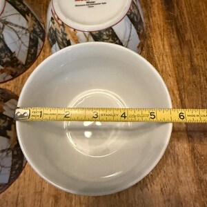 May include: A white ceramic bowl with a diameter of approximately 13 cm is measured with a tape measure. The bowl is part of a set with other bowls and mugs. The mugs have a camouflage pattern and the text "MOSSY OAK. Winter".