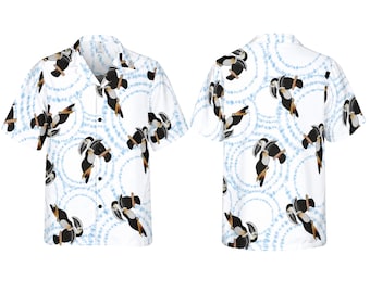 May include: A short-sleeved button-down shirt featuring a white background with a light blue circular tie-dye pattern and a repeating print of black and white toucans perched on brown branches. The shirt has a notched collar and black buttons.