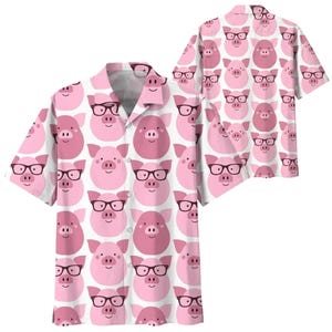 Puede incluir: Una camisa de manga corta con un estampado repetido de caras de cerdos rosas con gafas negras sobre un fondo blanco. La camisa tiene un cuello clásico y cierre de botones.