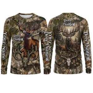 May include: A long-sleeve shirt featuring a camouflage pattern with a deer, a deer skull, and the text "Deer Hunting" and "Your Name". The design includes a forest background with brown, green, and tan tones, displayed from both front and back views.