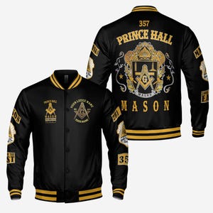 May include: Black and gold varsity jacket with Masonic symbols and text. The jacket features the words "Prince Hall" and "Mason" prominently displayed, along with other Masonic emblems and the number "357". The jacket has gold stripes on the collar, cuffs, and hem.