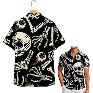Puede incluir: Camisa negra de manga corta con un estampado repetido de calaveras, huesos y globos oculares blancos. La camisa se muestra en una percha y la lleva una persona. La camisa tiene un cuello clásico y un corte holgado.