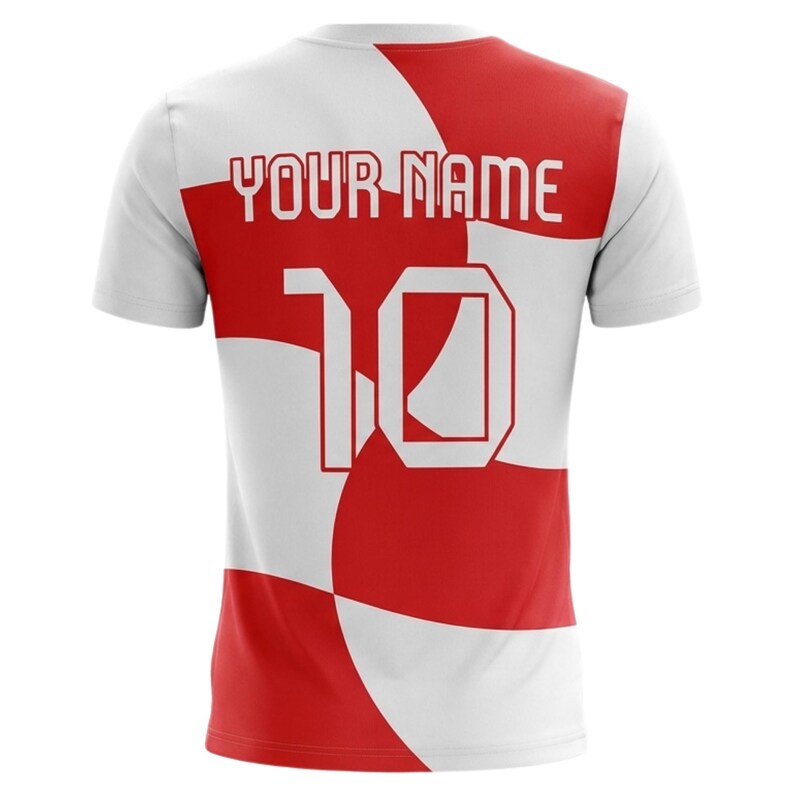 Pu&ograve; includere: Maglia a maniche corte bianca e rossa con la scritta "YOUR NAME" sopra il numero "10". La maglia ha un design geometrico con sezioni rosse e bianche. Il numero "10" &egrave; in grassetto, in bianco.
