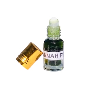 Puede incluir: Una pequeña botella de vidrio transparente con una etiqueta blanca que dice "ANNAH F". La botella contiene un líquido verde oscuro y tiene una tapa dorada. Tiene un aplicador de bola rodante.