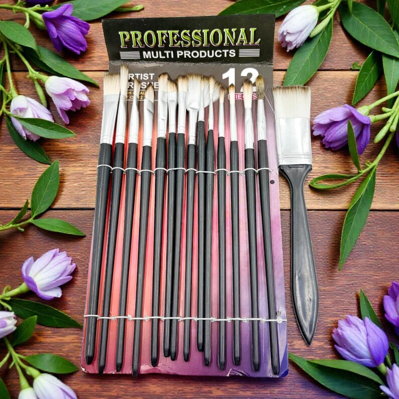May include: A set of 12 artist paint brushes with black handles and white bristles, packaged in a black and purple card. A larger brush with a black handle is also included. The package is on a wooden surface, surrounded by purple flowers.