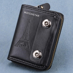 May include: Black leather wallet with a zip and snap closure. The wallet features the text "WATCHSTAR" and an embossed Eiffel Tower design with the year "1880". The wallet has a gold-coloured zip.