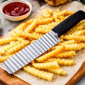 May include: A stainless steel crinkle cutter with a black handle rests on a wooden cutting board covered with parchment paper. The board is surrounded by golden crinkle-cut fries and a small bowl of red ketchup.