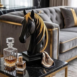 May include: A black horse head sculpture with gold detailing, displayed on a black marble table. A crystal decanter, perfume bottle, and patterned scarf are also on the table. A grey sofa with gold trim is in the background.