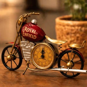 Könnte beinhalten: Eine dekorative Motorraduhr mit rotem Tank und goldenen Akzenten. Das Zifferblatt ist rund und mit römischen Ziffern versehen. Die Worte "Royal Enfield" sind auf dem Tank aufgedruckt.