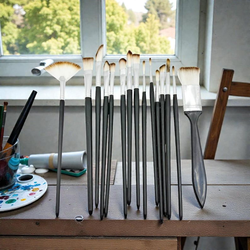 May include: A collection of artist paint brushes with black handles and white bristles, arranged on a wooden table. The brushes vary in size and shape, including a fan brush. A palette and paint tubes are visible in the background.