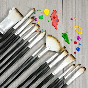 May include: An assortment of paint brushes with black handles and silver ferrules, arranged diagonally on a gray wooden surface. Splatters of yellow, red, green, purple, and blue paint are scattered around the brushes, suggesting artistic activity.