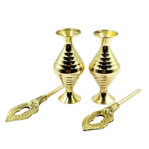 May include: Two gold-colored, ornate vases with a ridged design, paired with two matching applicators. The applicators have a decorative, leaf-shaped end. The items are set against a white background.