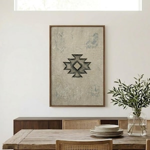 Op de afbeelding: Een ingelijst kunstwerk met een geometrisch ontwerp in grijstinten en zwart. Het kunstwerk hangt boven een donkerhouten dressoir. Een rustieke houten eettafel is gedekt met borden en omringd door stoelen met geweven rugleuningen.