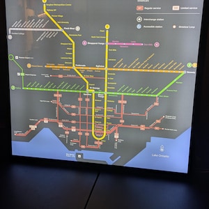 May include: A backlit map of the Toronto subway, light rail, and streetcar system. The map features colored lines representing different routes, with labels for stations and key landmarks. The map includes the text "Subway, Light Rail and Streetcar Map".