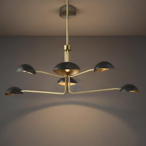 Op de afbeelding: Een moderne kroonluchter met een messing afwerking en zes zwarte, koepelvormige kappen. De armaturen zijn gerangschikt op gebogen armen die uit een centrale naaf komen, waardoor een stijlvol ontwerp ontstaat.