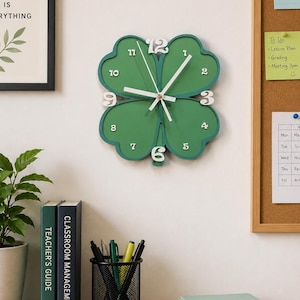 May include: A four-leaf clover shaped wall clock with a green face and white numbers. The clock features white hour, minute, and second hands centered on the clover. The numbers 3, 6, 9, and 12 are larger and raised, while the other numbers are smaller.