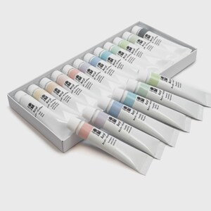 May include: A set of acrylic paint tubes in a white box. The tubes are white with colored caps and contain various pastel shades. The box is on a light gray background. The text "Acryl" is visible on the tubes.
