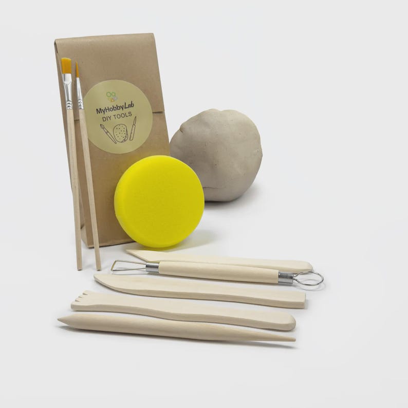 May include: A craft kit with a brown paper package, two paintbrushes, a yellow sponge, a ball of clay, and several wooden clay sculpting tools. The package has a sticker with the text "MyHobbyLab DIY TOOLS".