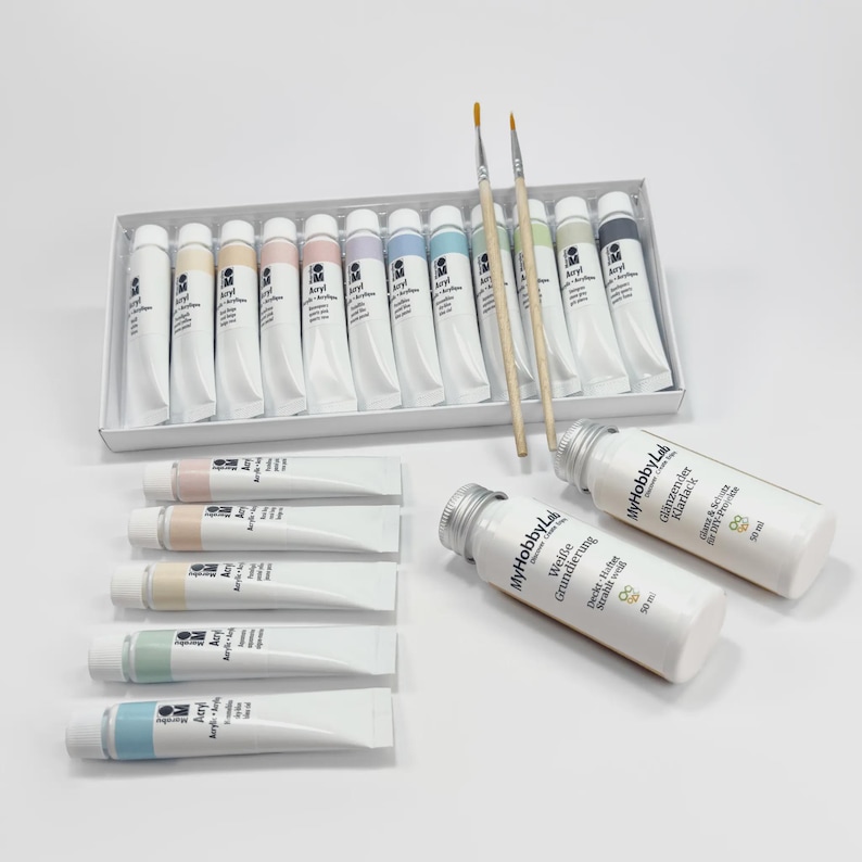 May include: A set of acrylic paints in a white box, with various pastel colors, and two paint brushes. Several tubes of paint are arranged separately. Two white bottles with silver caps are also visible.