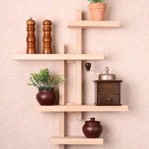May include: A light-coloured wooden wall shelf with multiple levels, holding decorative items. Items include two wooden salt and pepper shakers, two small potted plants, a coffee grinder, and a small brown jar with a lid.
