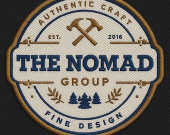 May include: Embroidered patch with a circular design. The patch features the text "AUTHENTIC CRAFT" and "FINE DESIGN" in a blue font. The center has the words "THE NOMAD GROUP" and crossed hammers. The patch also includes the year "2016".