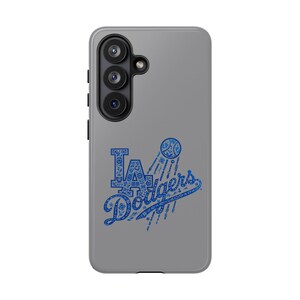 Könnte beinhalten: Eine graue Handyhülle mit dem Logo der Los Angeles Dodgers in Blau. Das Logo enthält die Buchstaben "LA" und das Wort "Dodgers" mit einer Baseball-Grafik. Die Hülle hat eine Dreifach-Kamera.