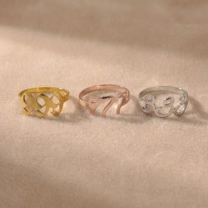 Op de afbeelding: Drie ringen in goud, ros&eacute;goud en zilver, elk met een ander nummerontwerp: 999, 777 en 333. De ringen worden gepresenteerd op een neutrale ondergrond, waardoor hun metallic glans wordt benadrukt.