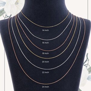 May include: A display of six delicate chain necklaces in varying lengths, from 35.5 cm to 61 cm. The chains are in gold, silver, and rose gold tones, presented on a black mannequin. Each chain is labeled with its length in inches.