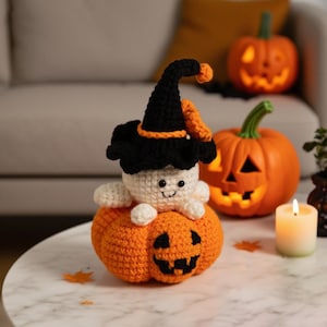 May include: A crocheted Halloween decoration featuring a white ghost wearing a black witch hat with orange accents, sitting atop an orange pumpkin with a carved face. The scene includes lit jack-o'-lanterns and a lit candle, creating a festive atmosphere.