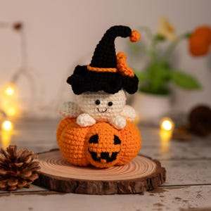 May include: A handmade crochet Halloween decoration. It features a white ghost wearing a black witch hat with orange trim, sitting on an orange pumpkin with a carved jack-o'-lantern face. The ghost has a smiling face. The decoration is on a wooden slice.