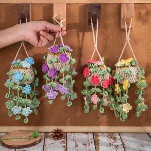 May include: Four handmade crochet hanging planters with colorful flowers. Each planter is a beige basket shape with a variety of flower colors, including blue, purple, pink, and yellow. The planters hang from a wooden board.