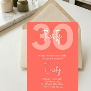 Puede incluir: Una tarjeta de invitación de cumpleaños de color coral con el número 30 y la palabra "thirty" en escritura blanca. La invitación incluye el nombre "Emily", detalles del evento y un número RSVP. La tarjeta está dentro de un sobre beige.