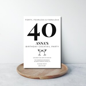 Puede incluir: Una tarjeta de invitación blanca con texto negro. La tarjeta incluye el texto "Forty, Fearless & Fabulous" y un gran "40". También incluye el texto "Anna's Birthday Cocktail Party" y los detalles del evento. La tarjeta está sobre una bandeja de madera.