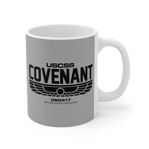 Puede incluir: Una taza de cerámica blanca con fondo gris. La taza presenta el texto "USCSS COVENANT" en negro, junto con un emblema estilizado y el texto "080417 WEYLAND-YUTANI CORPORATION."