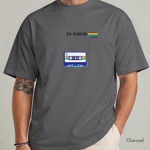 May include: Dark grey t-shirt featuring a cassette tape design with the text "ZX GAMER 1982" and a rainbow stripe. The shirt is made of a soft material. The colour of the shirt is charcoal.