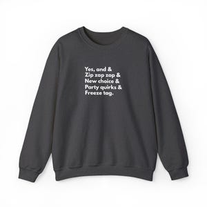 Könnte beinhalten: Dunkelgraues Sweatshirt mit dem weißen Text: "Yes, and & Zip zap zop & New choice & Party quirks & Freeze tag." Ein lässiger Rundhals-Stil.