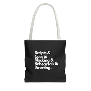 May include: Black tote bag with white text that reads "Scripts & Cues & Blocking & Rehearsals & Directing." The bag has white handles and is likely made of canvas or a similar material. The design is simple and text-focused.