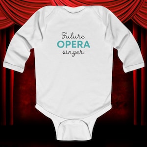 Könnte beinhalten: Weißer Baby-Body mit langen Ärmeln. Der Text "Future OPERA singer" ist in Türkis und schwarzer Schrift auf die Vorderseite gedruckt. Der Hintergrund zeigt einen roten Vorhang.