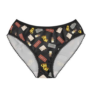 May include: Black underwear featuring a repeating pattern of theatre-related icons, such as playbills, theatre masks, and ticket stubs. The edges are trimmed with black lace.
