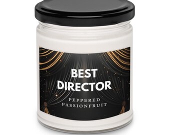 Peut inclure: Bougie en pot de verre blanc avec un couvercle noir. L'étiquette porte l'inscription "BEST DIRECTOR" sur un fond noir avec des accents dorés. Parfum "Peppered Passionfruit".