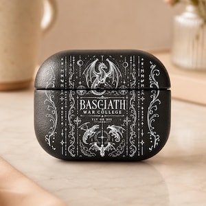 May include: A black protective case for wireless earbuds featuring a white graphic print. The design includes the text BASGIATH WAR COLLEGE FLY OR DIE, surrounded by intricate illustrations of dragons, celestial symbols, and decorative scrollwork.