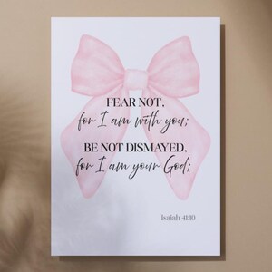 May include: A print featuring a watercolor illustration of a pink bow with the text "FEAR NOT, for I am with you; BE NOT DISMAYED, for I am your God; Isaiah 41:10" in elegant script. The artwork is on a white background.