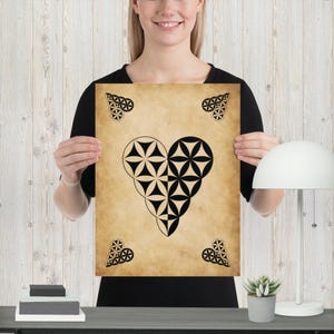 May include: A poster featuring a heart-shaped design composed of black geometric shapes on a tan background. The poster has four corner heart designs. The poster is held by a person.