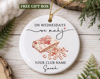 May include: A round white ceramic ornament featuring a gold hanging string. The design includes the text ON WEDNESDAYS we mahj with a small heart, a red and white illustration of a mahjong tile pouch, and the text YOUR CLUB NAME and Sarah.