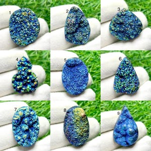 Peut inclure: Une collection de neuf cabochons en pierre druzy bleu irisé, numérotés de un à neuf, présentant des surfaces cristallines texturées avec des reflets dorés et verts scintillants dans diverses formes, notamment ovales, poires et gouttes.
