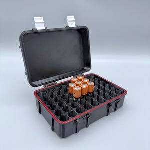 Peut inclure: Boîtier de rangement de piles noir ouvert, avec un liseré rouge, contenant des piles AA. Le boîtier a des loquets blancs et une poignée. Les piles sont orange et noires. Le boîtier est conçu pour contenir plusieurs piles.