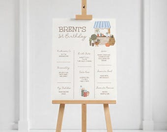 May include: A printable poster for a first birthday party with a cute illustration of a market stall. The poster has a list of information about the birthday child, including their nickname, birth date, favorite food, and favorite things. The poster is designed in a rustic style with brown and white colors.
