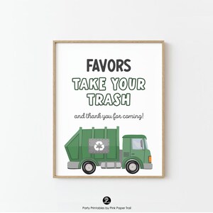 May include: A framed print with the text "FAVORS TAKE YOUR TRASH and thank you for coming!" above a green garbage truck illustration. The print has a white background and a wooden frame. The garbage truck has a recycling symbol.