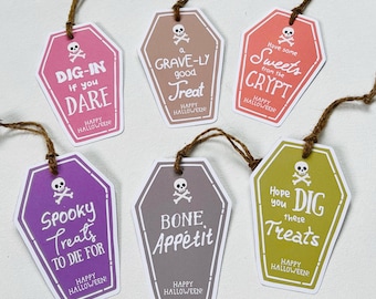 May include: Six coffin-shaped Halloween gift tags with brown twine. Each tag has a different color and phrase, including "Dig-In if you Dare" and "Spooky Treats to Die For." Each tag has a skull and crossbones and says "Happy Halloween!"